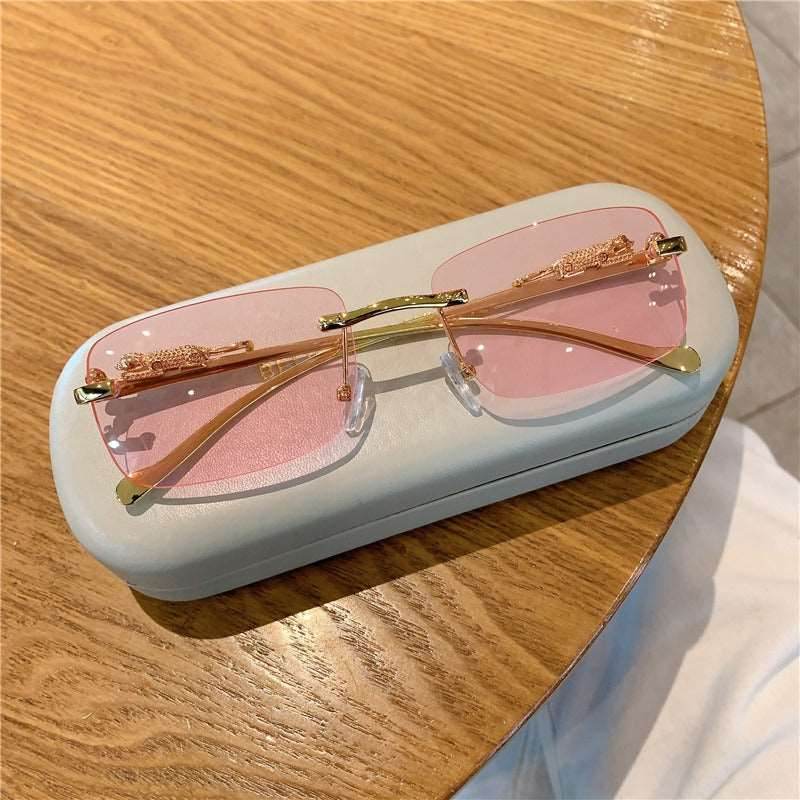 Sunglass Lover trendy rimless sunglasses for women pink lens gold temples on white case on wood table