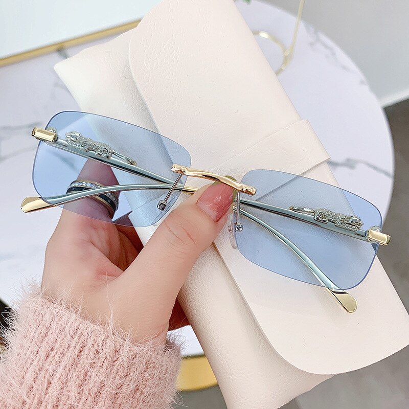 Sunglass Lover rimless sunglasses for men with blue lenses and gold accents held above white case