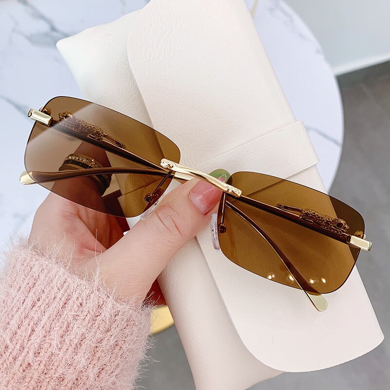 Brown lens rimless sunglasses for men with gold accents held over a white case