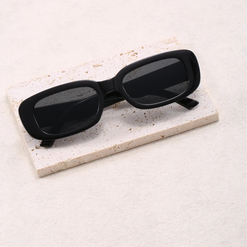 Jimmy Rectangle sunglasses by Sunglass Lover in black with dark lenses on a light stone surface