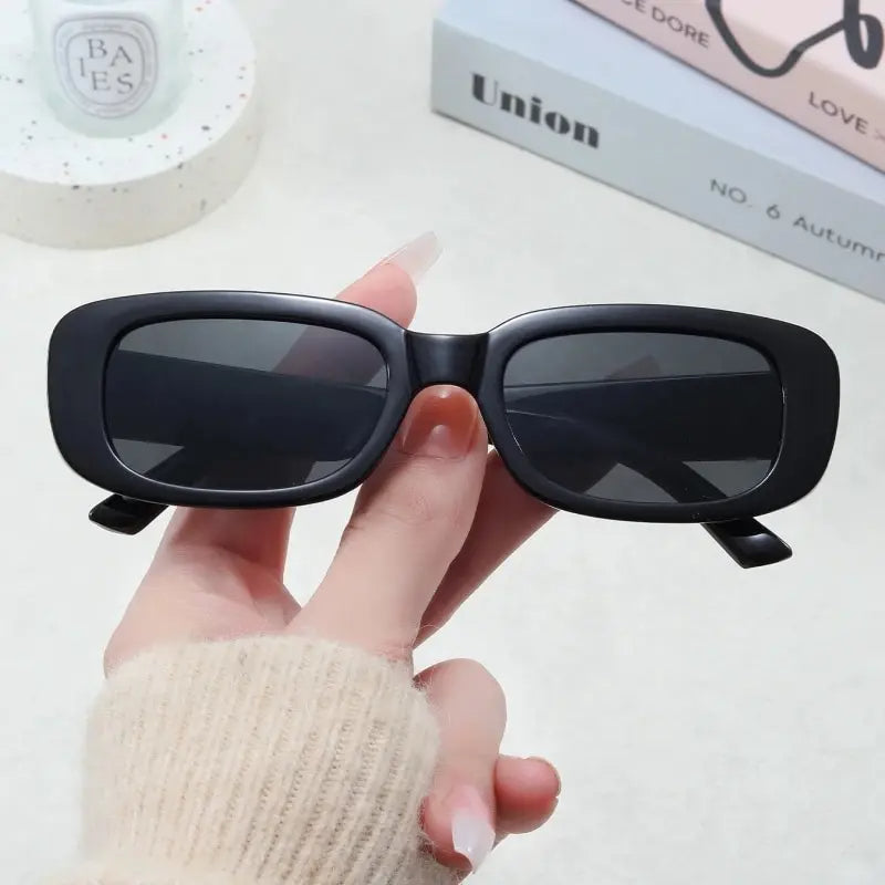 Jimmy Rectangle sunglasses in black held by hand with cream sweater background by Sunglass Lover