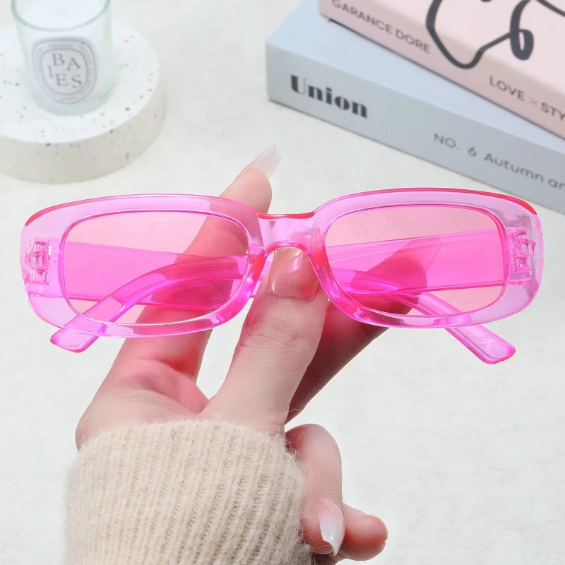 Jimmy Rectangle sunglasses in transparent pink held by hand with books and candle background