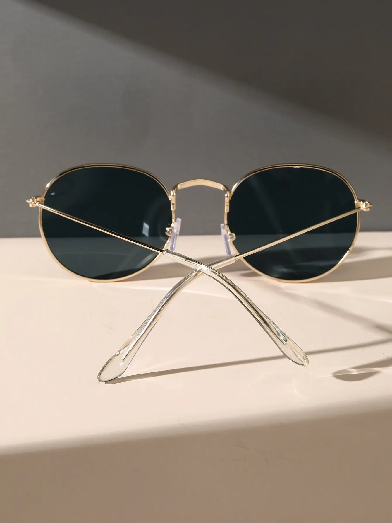 Sunglass Lover oval sunglasses for men with gold frames and dark lenses on beige surface