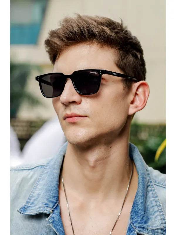 Young man wearing small black rectangle sunglasses by Sunglass Lover with denim jacket outdoors