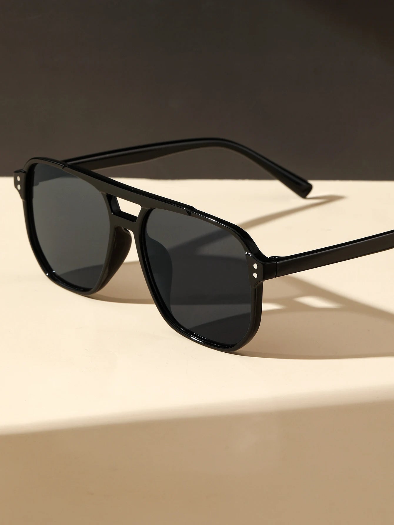Black square geometric street sunglasses with dark lenses from Sunglass Lover on a beige surface