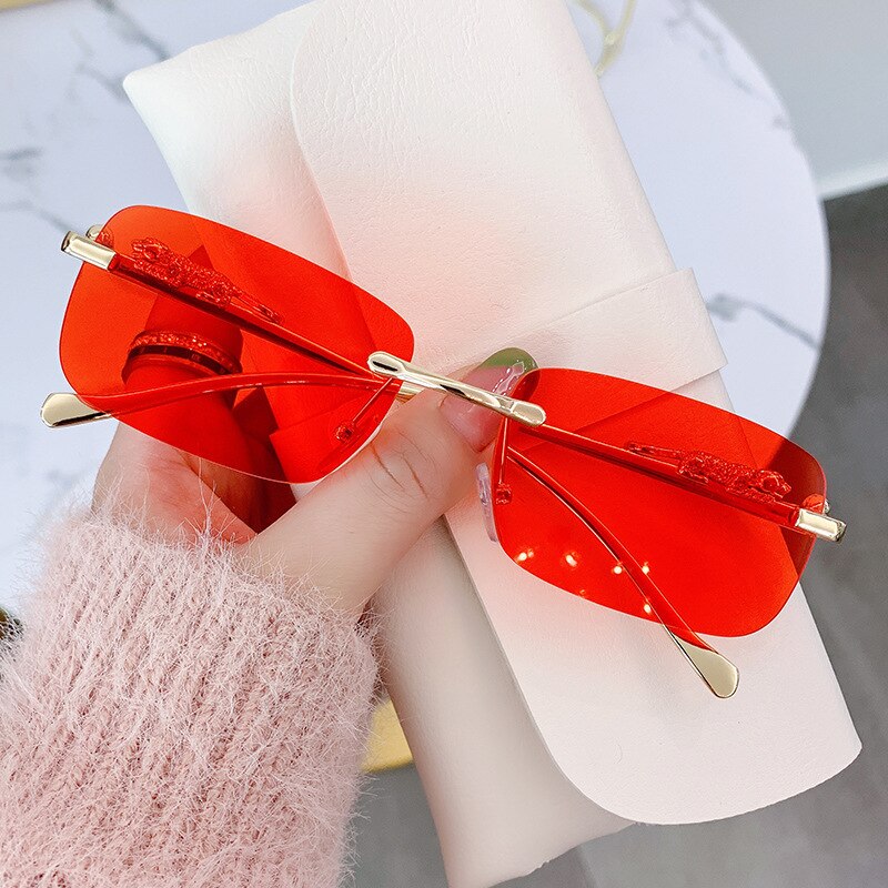 Red rimless sunglasses for men with gold temples held above a white leather case
