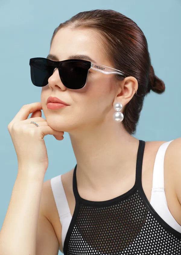 Woman wearing Risen Blaze Weyfarer sunglasses with black lenses clear temples pearl earrings against blue