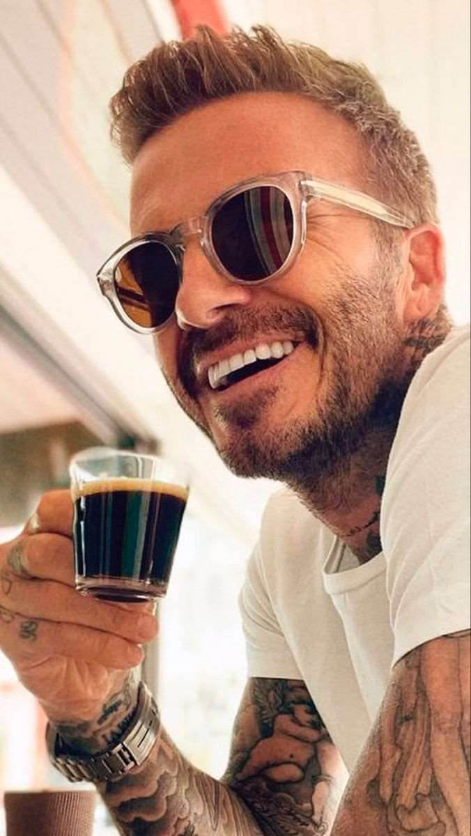 Man wearing steampunk round sunglasses with clear frames sipping espresso tattooed wrist smiling
