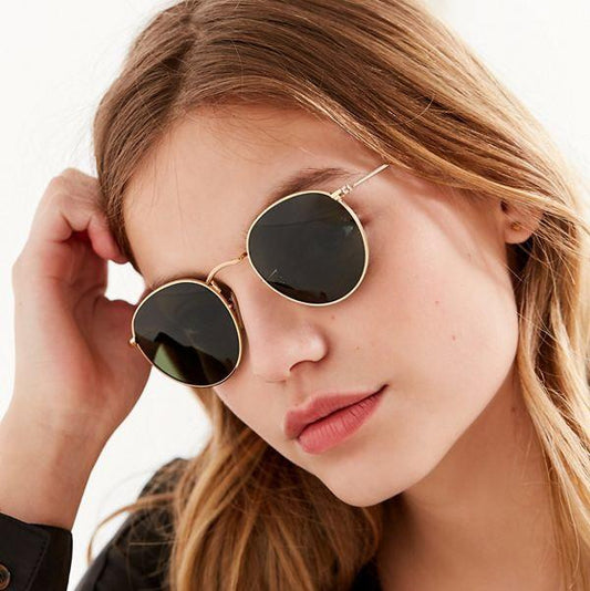 Woman wearing round vintage style sunglasses online with gold metal frame and dark lenses
